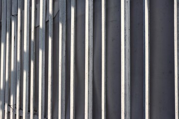 Obraz premium A close-up of vertical metal bars on a wall or gate, painted in a slightly weathered white tone with shadows creating a dramatic pattern across the surface.