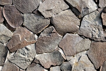 Close-up texture of a natural stone wall built with irregular rock pieces tightly arranged together, showcasing rugged surfaces, earthy tones, and raw durability.