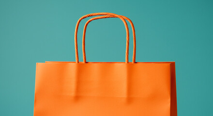 Close up of an orange shopping bag with rope handles against a teal background studio shot