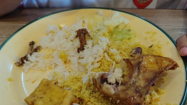 Close-up of a traditional meal with rice and fried chicken eaten by hand. Authentic Asian food culture showcasing local dining habits and the joy of eating with fingers. 
