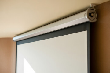 Retractable projection screen mounted on beige wall in modern indoor conference room with natural light and blank display surface