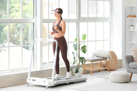 Sporty young woman in VR glasses exercising on treadmill at home - Powered by Adobe