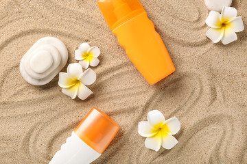 Obraz na płótnie Canvas Plumeria flowers with bottles of sunscreen and spa stones on sand