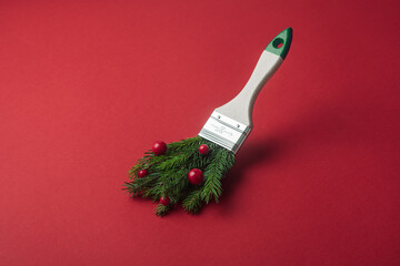 Paintbrush with fir branches and red berries creates a festive Christmas mood on bright red background as a creative holiday concept.