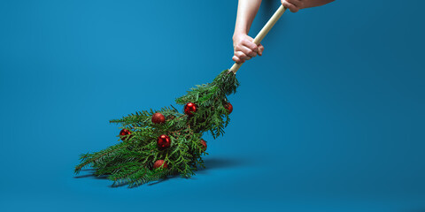 Hands hold a festive evergreen broom with red ornaments on blue background, leaving copy space for Christmas banner or winter sale.