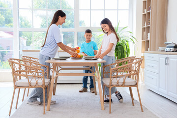 Young mother with her children setting dining table in kitchen