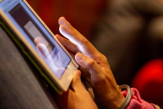 A person's hand is shown in a close-up, gently touching the glowing screen of a digital tablet. The shot represents modern technology and digital connection.