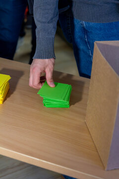 A hand selects a green sticky note from a pile on a wooden table, symbolizing idea generation, brainstorming, or a business planning session.