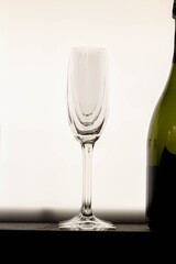 An empty, elegant champagne glass stands beside a bottle, with a clean and bright white background. A symbol of upcoming celebration.