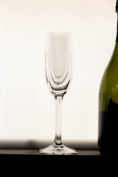 An empty, elegant champagne glass stands beside a bottle, with a clean and bright white background. A symbol of upcoming celebration.