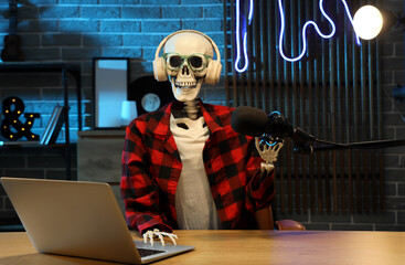Human skeleton model with laptop at table in dark podcaster's studio