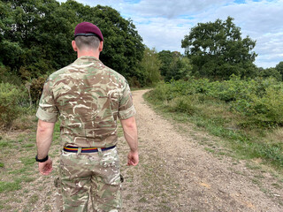 Close-up UK Army officer in maroon beret, REME stable belt, standing arms down, back to camera in woodland, British military personnel in field.
