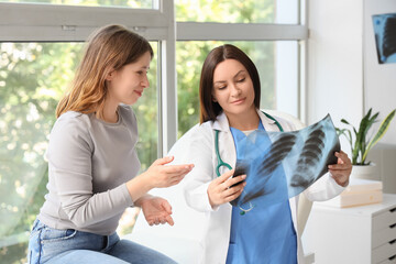 Fototapeta premium Female doctor showing x-ray image of lungs to patient at hospital