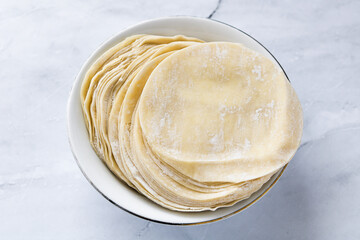 Top view of a stack of round and thinly dumpling wrappers or skins, lightly dusted with flour and ready for use. These dough creates a variety of dishes such as dumplings, gyozas, and wonton. 