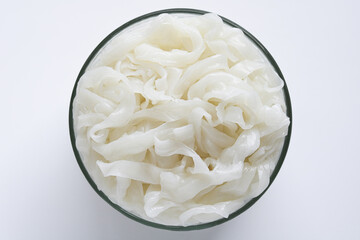 Top view of a clear glass bowl filled with raw and uncooked kway teow (fresh flat rice noodles),...