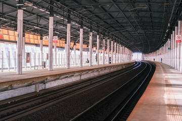 Empty modern train station platform with covered roof and curved tracks. Public transportation infrastructure. Travel and journey concept.