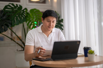 Asian freelancer working remotely from coffee shop using tablet and taking notes