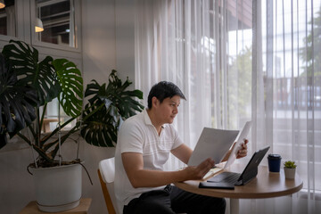Asian freelancer comparing documents at home office desk