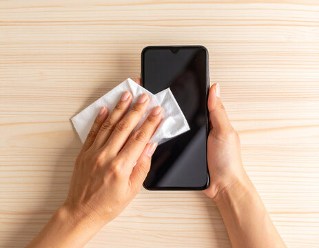 Cleaning Black Smartphone Screen with White Wipe on Wooden Table - Powered by Adobe
