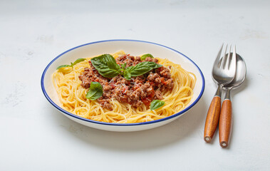 Delicious spaghetti bolognese is garnished with fresh basil leaves and parmesan, served on a white plate next to cutlery on a napkin top view