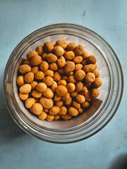 Top view of a glass jar filled with crunchy coated peanuts snack on textured background. Delicious traditional food, salted nuts, party snack, and tasty appetizer for lifestyle or culinary concept.