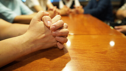 People sitting around table with folded hands, prayer or study meeting