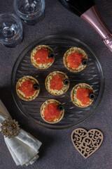 Festive tartlets with red caviar, egg and melted cheese, decorated with black olives, Top view