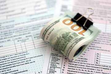 Big amount of United States USD dollar bills on table with 1040 tax return form