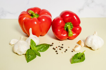 Fresh red bell peppers, garlic, basil and black peppercorns on kitchen table. Culinary ingredients for cooking, healthy food, organic vegetables, gastronomy, spice concept.