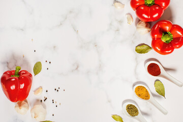 Bright spices in spoons arranged in a semicircle with red peppers, garlic and bay leaves on marble background. Food composition and background for spice and vegetable advertising.