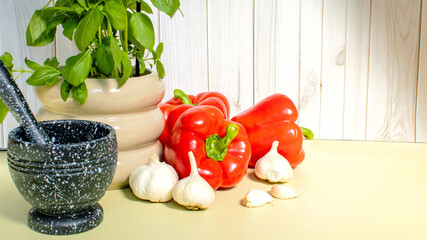 Culinary composition with spoons of bright spices for flavor, garlic in mortar and fresh vegetables on olive background. Natural ingredients, food background, healthy cooking and advertising.