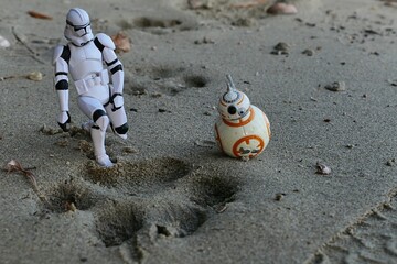 Fototapeta premium Star Wars model of Clone Trooper with astromech ball shaped droid BB-8 examining track of huge dog in wet sand on bank of Danuber river, southern Slovakia. 