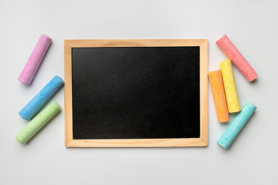 Black chalkboard in wooden frame, multicolored chalks on light background top view. Empty school board, menu board in restaurant, cafe. Free space for your inscription. School student mockup