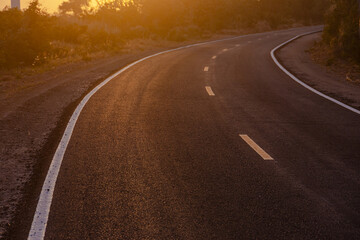 Fototapeta premium Black asphalt curve road, two lane curved along way path forward at countryside sunset sky