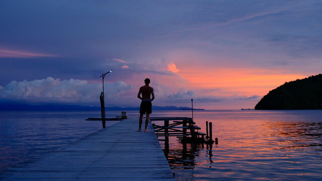 Colorful sunset over tropical islands with orange and purple sky reflecting on the calm sea in Raja Ampat, Indonesia symbol of travel and relaxation