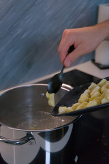 A person uses a spoon to slide raw potato gnocchi from a baking sheet into a pot of boiling water on a stove.