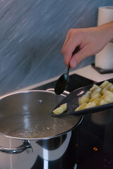 A person uses a spoon to slide raw potato gnocchi from a baking sheet into a pot of boiling water on a stove.