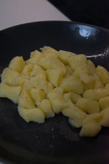 A pile of freshly cooked potato gnocchi is shown on a dark gray plate, ready to be served.