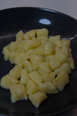 A pile of freshly cooked potato gnocchi is shown on a dark gray plate, ready to be served.