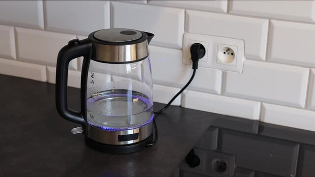 A transparent electric kettle with steel inserts and boiling water with neon lighting on the table of a stylish kitchen. Boiling water in an electric kettle.