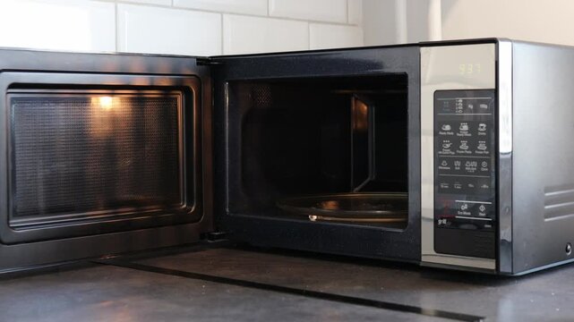 A mirrored microwave oven in a stylish kitchen. A girl opens the microwave and closes it.