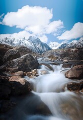 Mountain Stream Flowing Through Rocky Landscape with Snow-Capped Peaks and Dramatic Sky