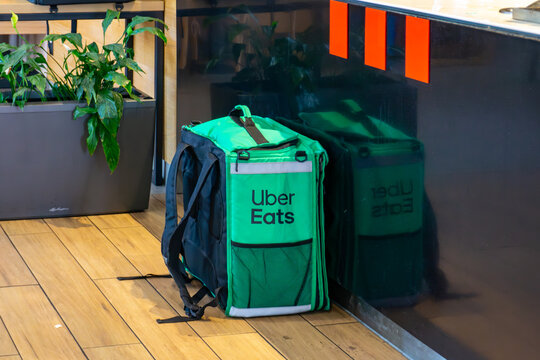 Green Uber Eats delivery backpack placed on the floor inside a restaurant near counter and plant