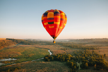 Hot air balloon flying over green landscape at sunrise