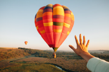 Tourist reaching for colorful hot air balloon during flight at sunset
