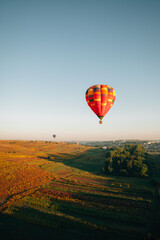 Hot air balloon flying over cultivated fields at sunrise