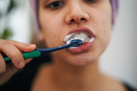 A woman brushes her teeth with a toothbrush and toothpaste, focusing on oral hygiene. Her hand holds the brush, creating foam around her mouth. This image captures a daily routine.
