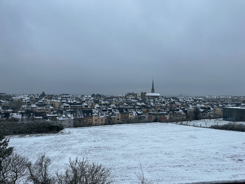Flat plot ready for construction, covered in snow, with an aerial view of a residential neighborhood in Luxembourg in winter.