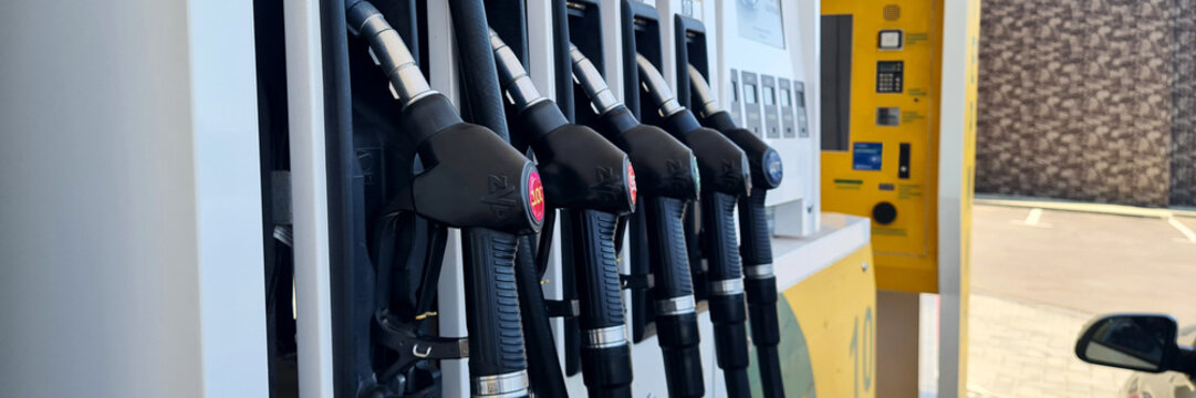 Gasoline pumps at a fuel station with multiple nozzles and a digital display. The background shows a brick wall and clear sky.