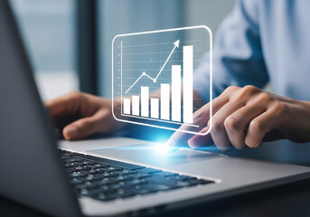 Close up of a person s hands interacting with a glowing digital bar graph and line chart overlay on a laptop keyboard demonstrating financial growth and data analysis
